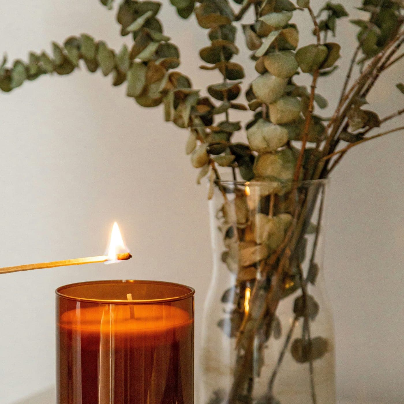 Oud Premium Candle — An amber jar candle being lit beside a glass vase of eucalyptus
